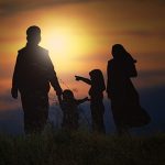 Siluet ibu bapa bersama dua anak di luar rumah ketika matahari terbenam