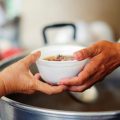 Tangan menghulurkan semangkuk makanan kepada penerima, sebagai gambar hiasan bantuan.