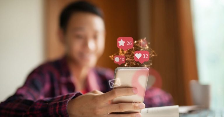 Person holding a smartphone with social media notification icons (like, comment, and save) floating above the screen.