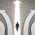A man in a suit walks toward a bright upward arrow between four diverging curved paths, symbolizing choosing a direction.