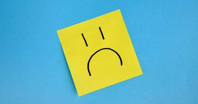 Yellow sticky note with a simple sad face drawn in black on a blue background.