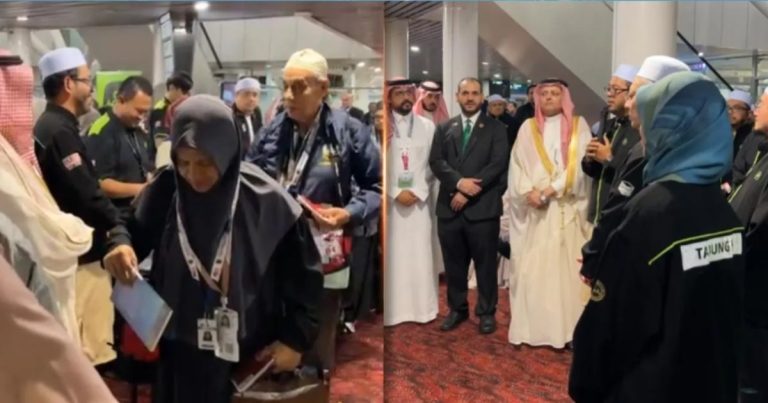 Group of dignitaries and attendees in traditional robes and suits stand in an indoor event space, many wearing name badges and lanyards.