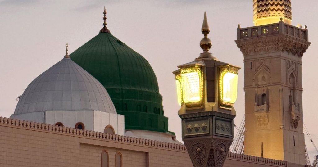 Green-domed and white-domed mosque with a decorative street lamp near a minaret at dusk