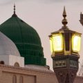 Green-domed and white-domed mosque with a decorative street lamp near a minaret at dusk