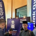 Group of men at an indoor expo booth with Think Quran display and tall blue banners reading Think Quran.