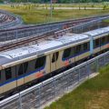 Modern silver-beige rapidKL passenger train on elevated tracks, curving rail lines in the background and green fields around the station area.