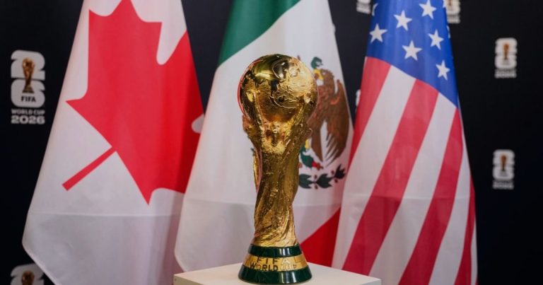 Gold FIFA World Cup trophy on a pedestal, with the Canadian, Mexican, and United States flags in the background.