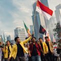 Group of protesters marching in a city street, holding colorful flags under skyscrapers in the background.