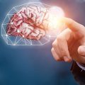 Hand in a suit finger-touches a glowing brain outlined by a geometric network, symbolizing AI or neural interfaces.