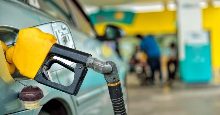 Close-up of a yellow gas pump nozzle inserted into a car at a gas station.