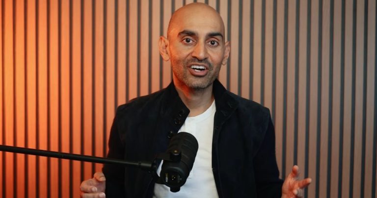 Strategi Media Sosial 2026: Kuasai GEO Cara Neil Patel | Denaihati Bald man speaking into a microphone in a studio with orange lighting and vertical panel backdrop on the wall.