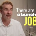 Man in a white shirt sits at a microphone during a recording, with the text overlay: 'There are a bunch of JOBS'.