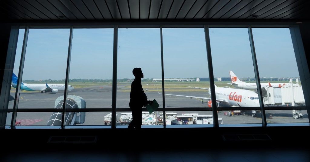 Silhouette of a traveler with a bag walking along a terminal window overlooking planes on the tarmac.]','Silhouette of a person carrying a briefcase or bag, seen against large windows at an airport gate with airplanes outside.