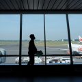 Silhouette of a traveler with a bag walking along a terminal window overlooking planes on the tarmac.]','Silhouette of a person carrying a briefcase or bag, seen against large windows at an airport gate with airplanes outside.