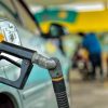 Close-up of a yellow gas pump nozzle inserted into a car at a gas station.